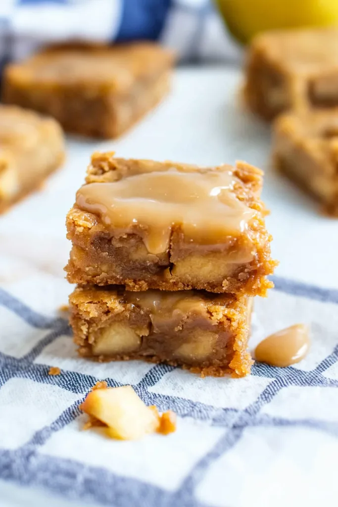 A golden square dessert bar topped with glossy maple glaze, showing tender apple chunks inside.