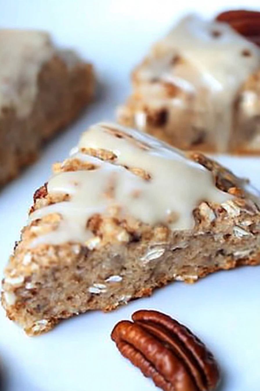 Freshly baked oat scones topped with maple glaze and crunchy pecan pieces on a serving plate .