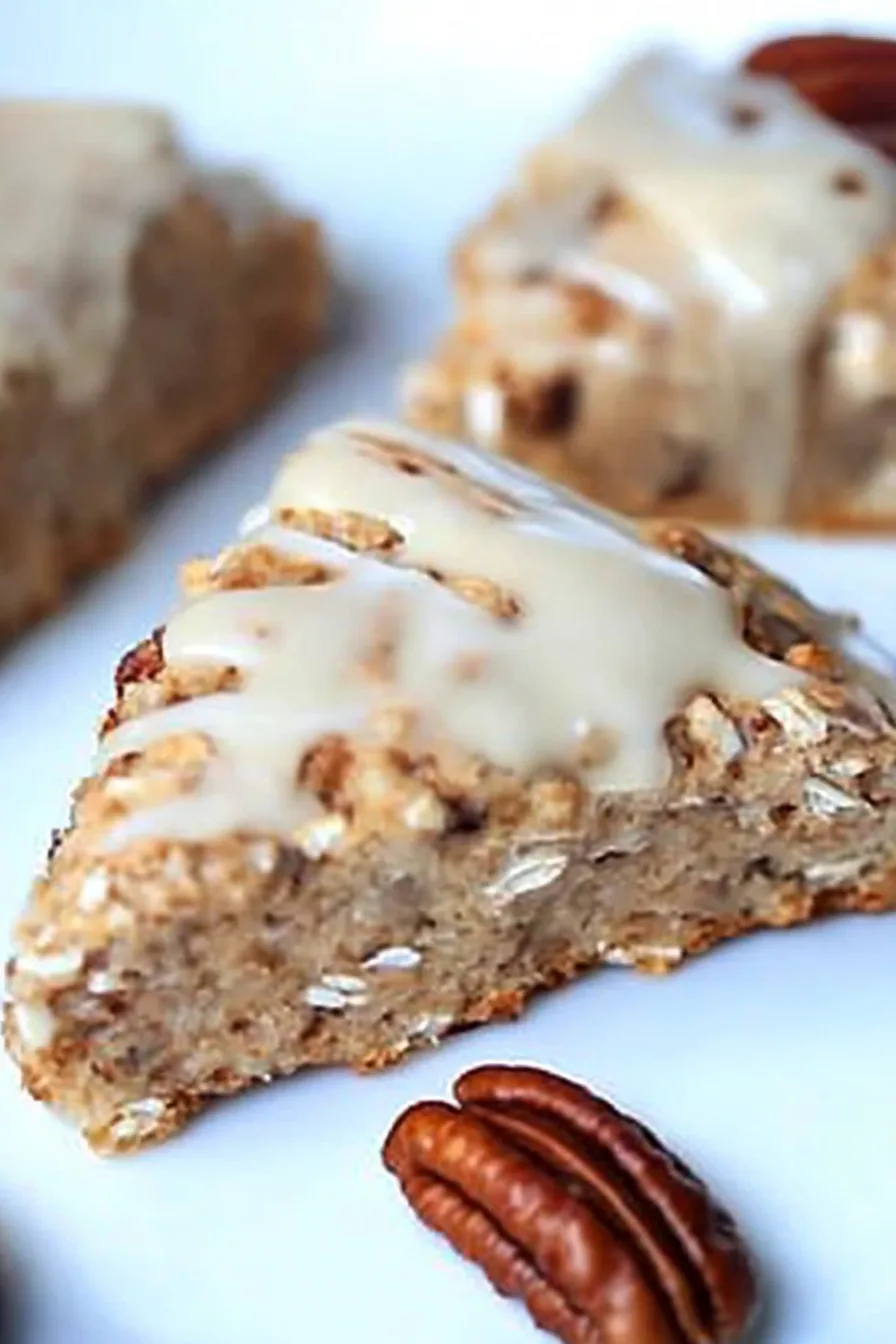 Freshly baked oat scones topped with maple glaze and crunchy pecan pieces on a serving plate .