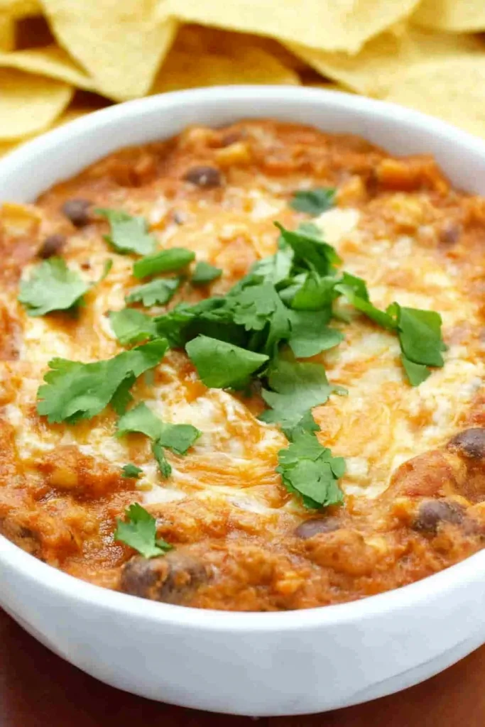 Baked dip with a golden cheese layer, garnished with fresh cilantro leaves.