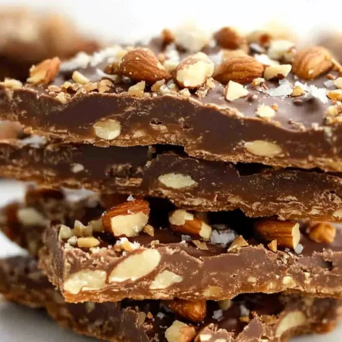 Stacked pieces of crunchy toffee topped with coarse salt and chopped nuts.