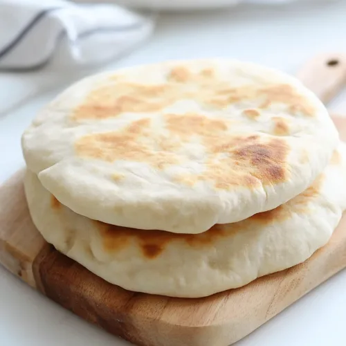 Two pieces of warm bread arranged on a white surface with herbs nearby.