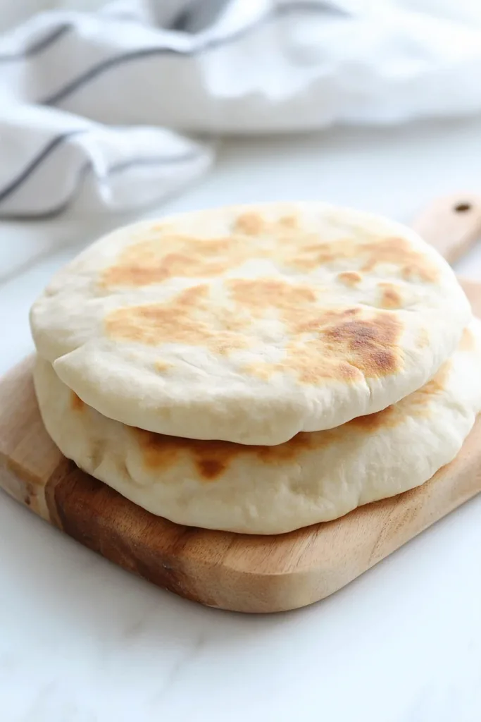 Two pieces of warm bread arranged on a white surface with herbs nearby.