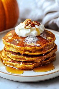 Stack of fluffy golden pancakes topped with whipped cream and pecans.