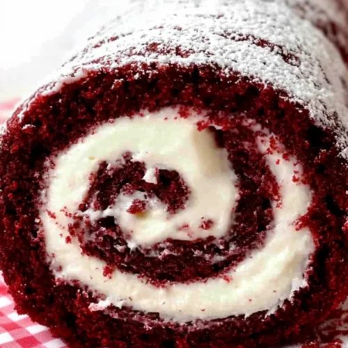 Cake roll resting on checkered cloth, highlighting red and white contrast.