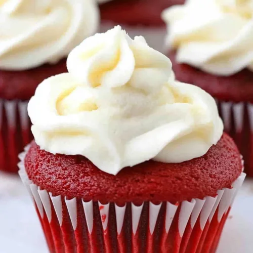 Cupcake in a paper liner with smooth cream cheese frosting, others blurred in the background.