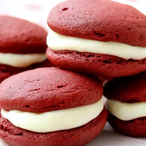 Stack of deep red sandwich cookies with creamy white filling.