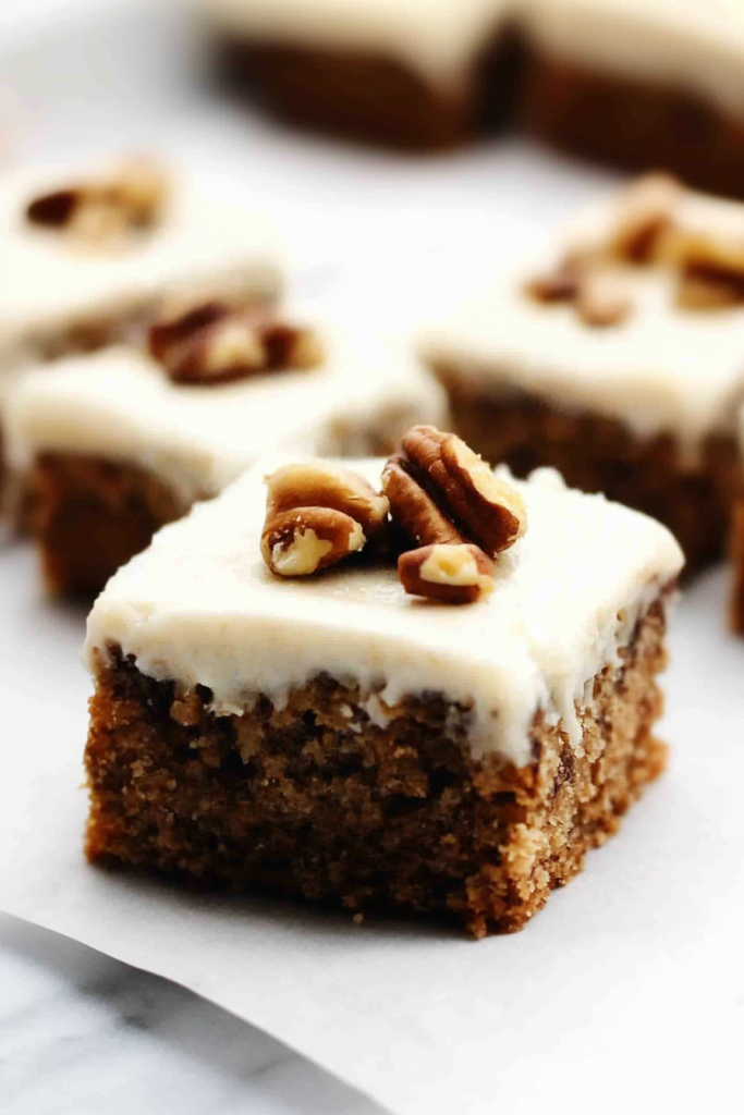 Square dessert bar topped with creamy frosting and chopped pecans.