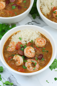 Close-up of rich stew highlighting shrimp, sliced sausage, and fresh herbs.