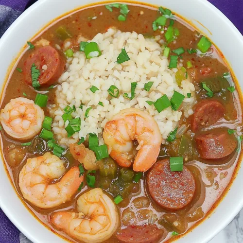 Hearty bowl of gumbo with rice in the center, surrounded by sausage, shrimp, and vegetables.