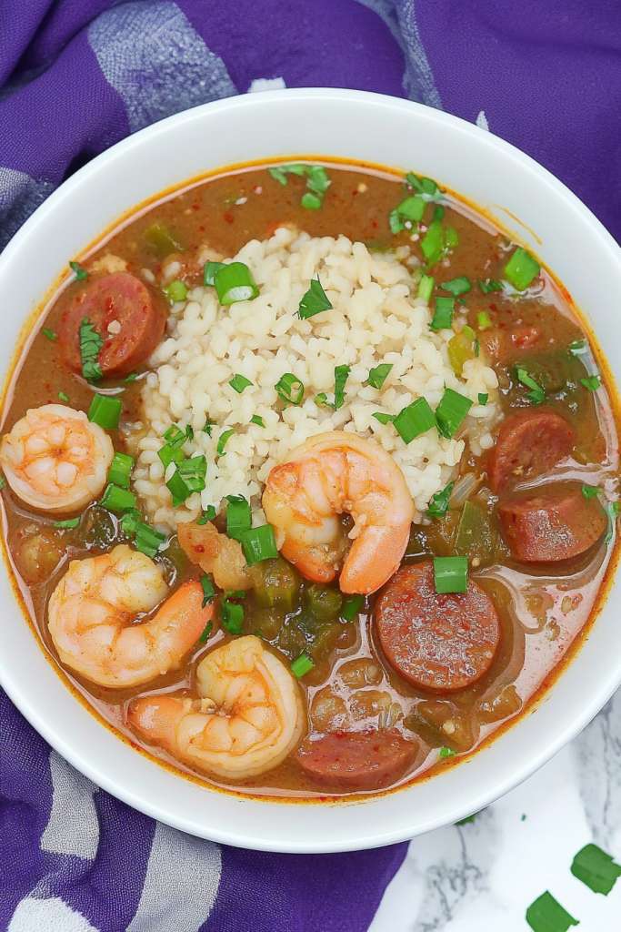 Hearty bowl of gumbo with rice in the center, surrounded by sausage, shrimp, and vegetables.