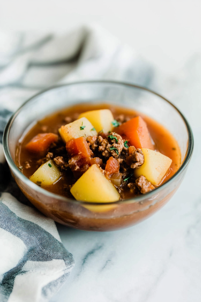 Glass bowl filled with hearty stew of carrots, potatoes, and ground meat.