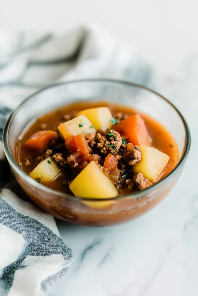 Glass bowl filled with hearty stew of carrots, potatoes, and ground meat.