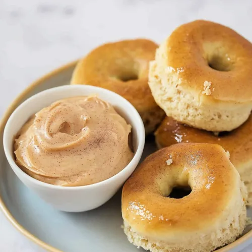 Golden brown dinner rolls stacked on a plate beside a creamy cinnamon butter dip.