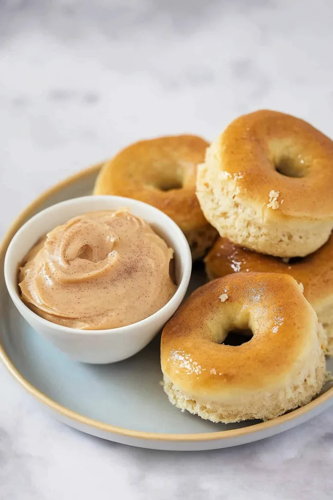 Golden brown dinner rolls stacked on a plate beside a creamy cinnamon butter dip.