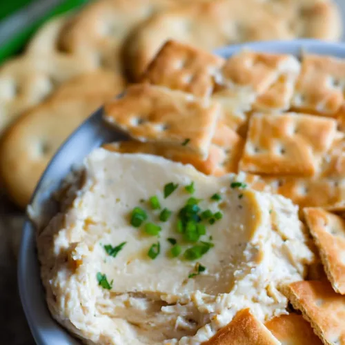 Smooth homemade appetizer dip topped with herbs and surrounded by crisp snack crackers