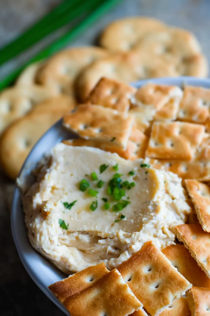 Smooth homemade appetizer dip topped with herbs and surrounded by crisp snack crackers