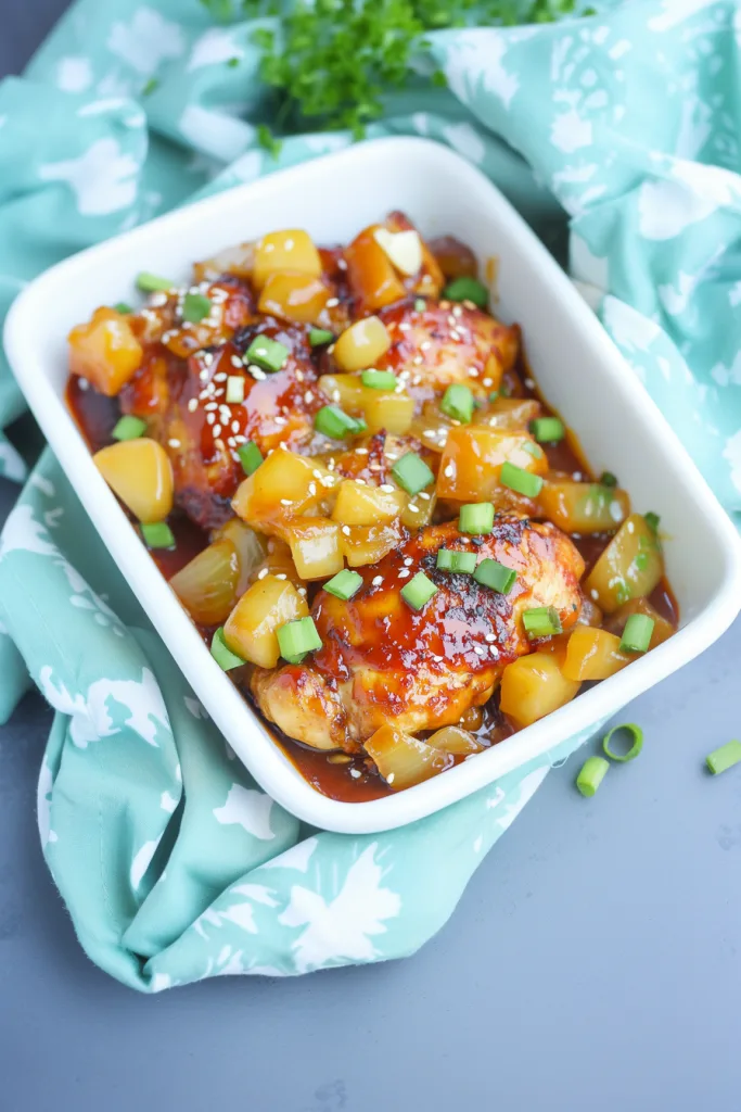 White serving dish filled with saucy chicken, styled with bright toppings for contrast.