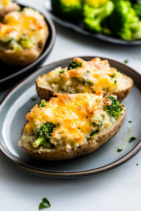 Golden cheese-topped potato skins loaded with broccoli and served on a gray plate.