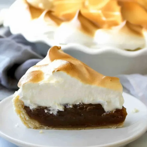 Slice of rich chocolate-filled pie topped with toasted meringue on a white plate.