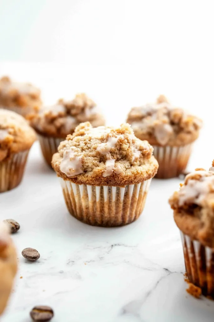 Golden muffin topped with crumbly streusel and light glaze in a paper liner.
