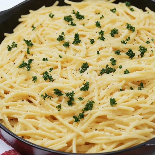 Skillet of spaghetti coated in creamy white sauce with parsley garnish