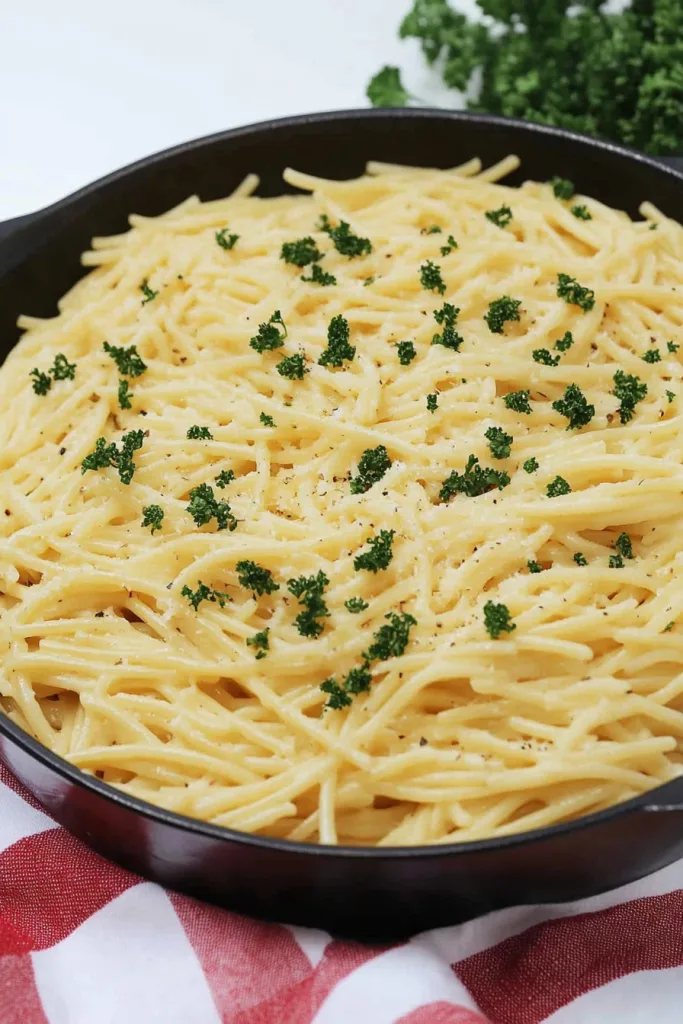 Skillet of spaghetti coated in creamy white sauce with parsley garnish