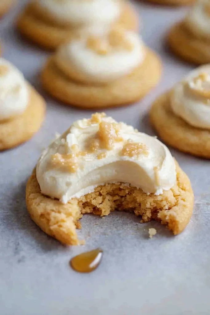 Soft cookie with a bite taken out, topped with creamy frosting and sugar crumbs.