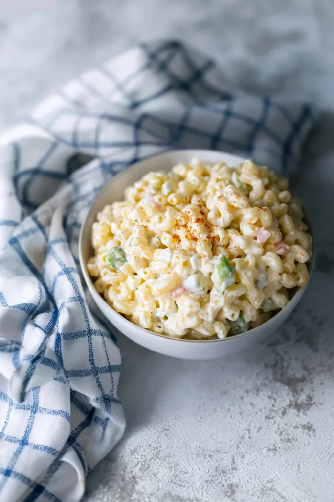 Creamy macaroni salad in a white bowl with diced celery and red bell pepper.