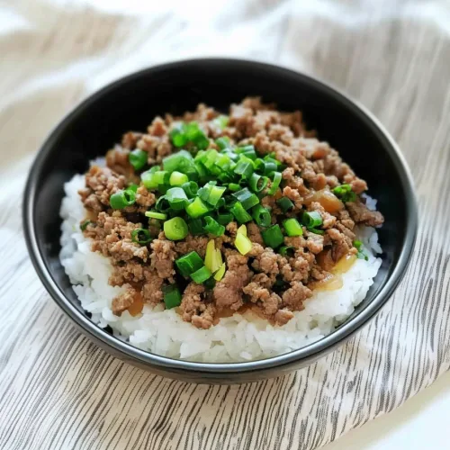 A serving of rice and beef with chopped green onions on a striped cloth background.