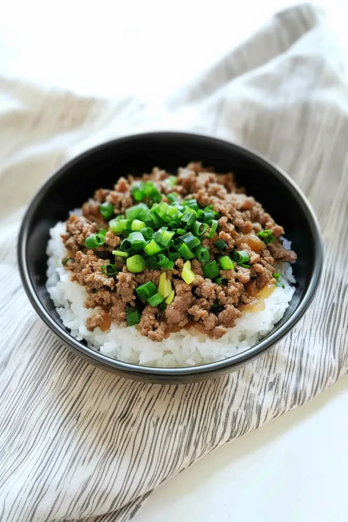 A serving of rice and beef with chopped green onions on a striped cloth background.