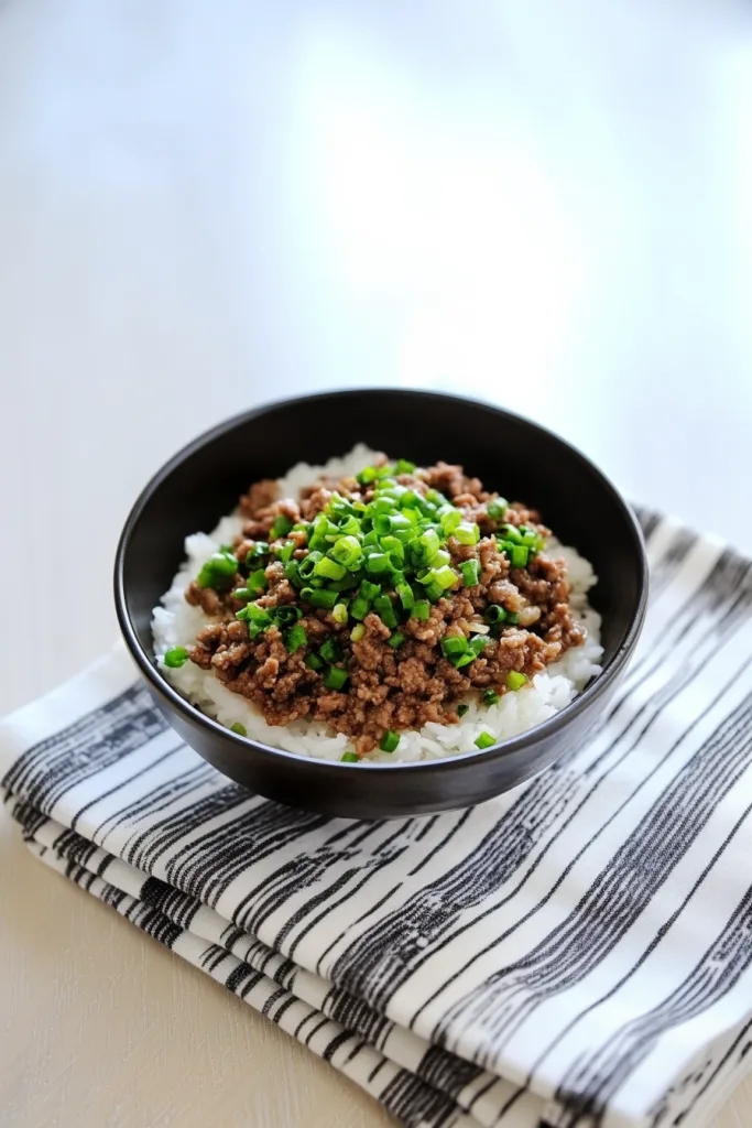 Black bowl of white rice topped with seasoned ground beef and green onions.