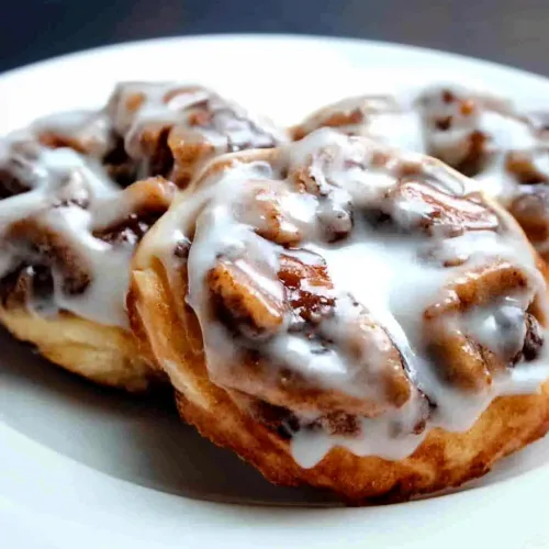 Three golden rolls topped with glossy white icing on a plate