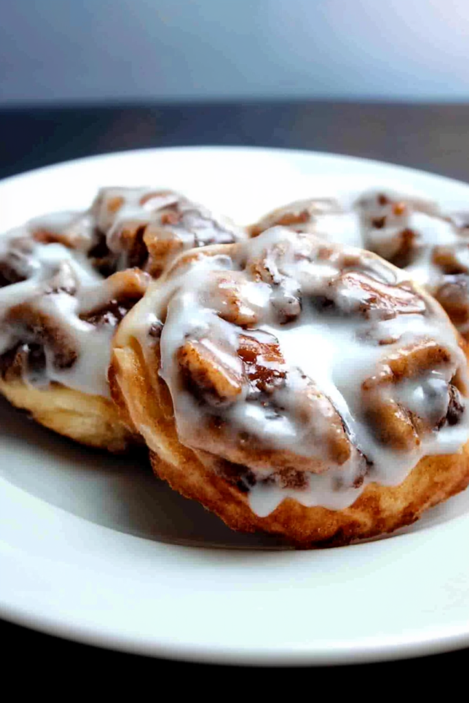 Three golden rolls topped with glossy white icing on a plate