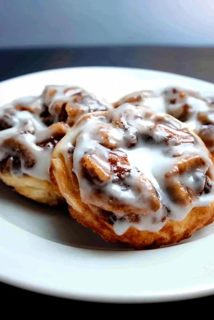 Three golden rolls topped with glossy white icing on a plate