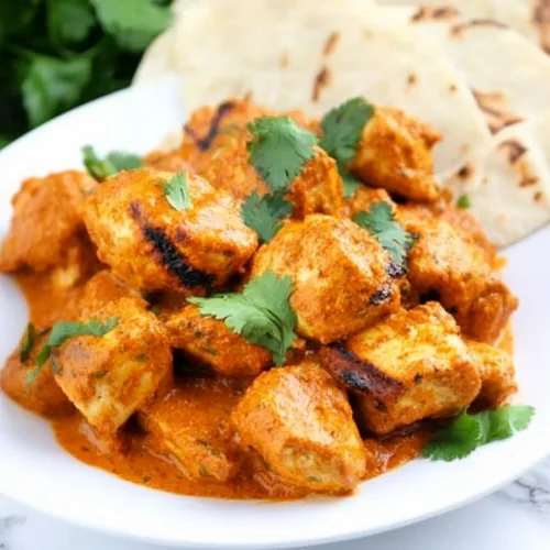 Plate of tender chicken pieces coated in a creamy orange sauce, topped with fresh cilantro.