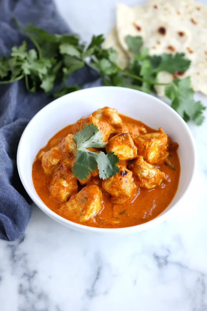 Golden chicken chunks simmered in a glossy spiced sauce, styled with herbs for garnish.
