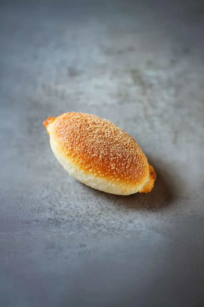 Ovalโshaped bread roll with a glossy finish, sprinkled lightly with crumbs.