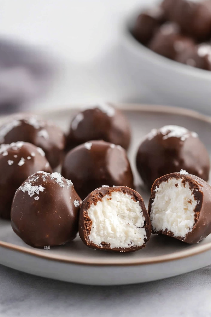 Close-up of glossy chocolate balls with textured coconut interior peeking through a sliced piece.