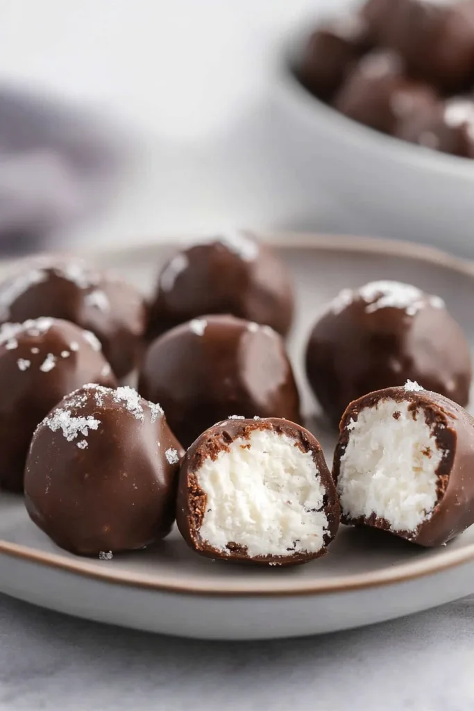 Close-up of glossy chocolate balls with textured coconut interior peeking through a sliced piece.