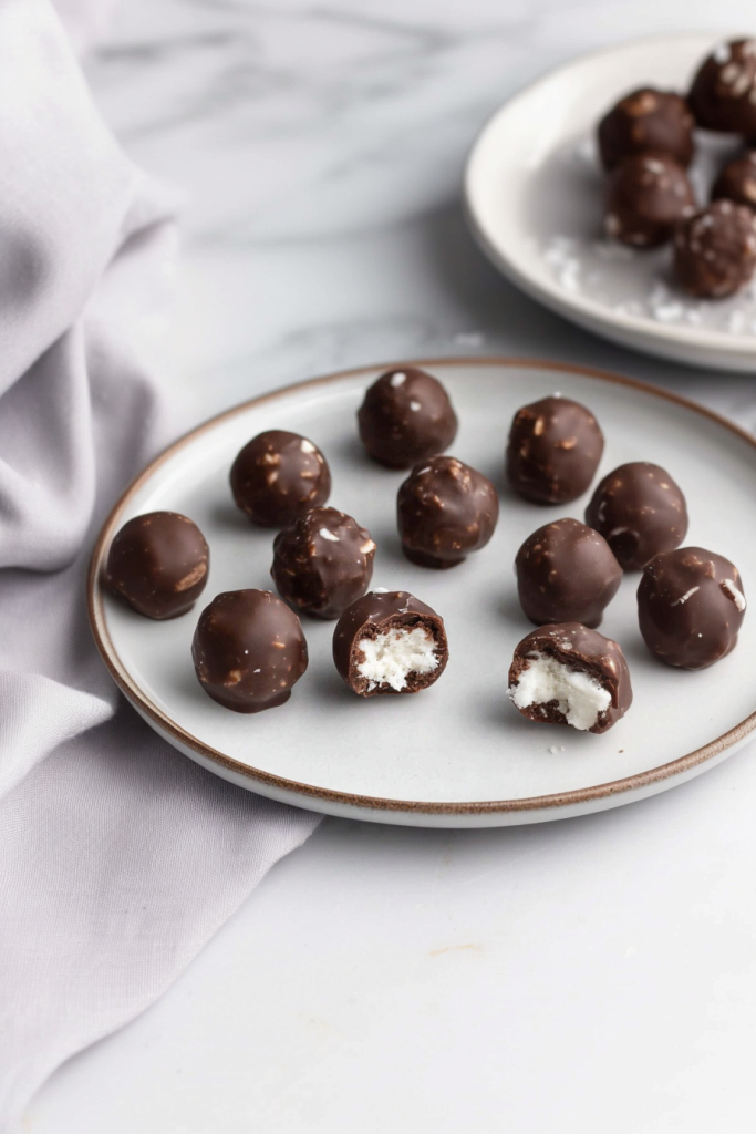 Plate of round chocolate treats, smooth coating contrasted by flaky filling inside.