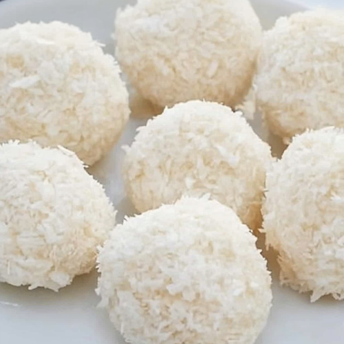 Round coconut-covered treats on marble, with one showing a creamy bite inside.