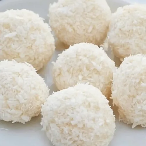 Round coconut-covered treats on marble, with one showing a creamy bite inside.