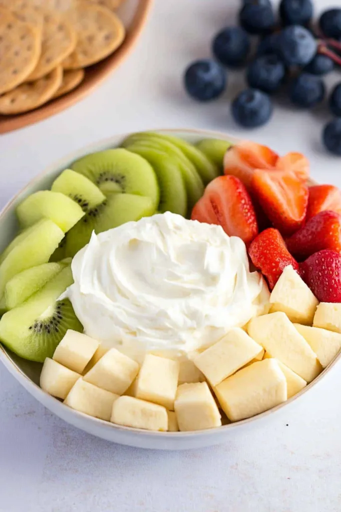 Snack platter featuring a white dip in the center with fruit slices and crackers arranged neatly around it