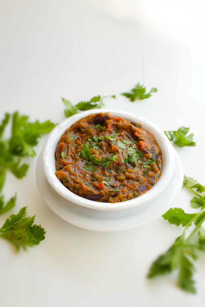 Warm eggplant and tomato stew presented in a simple white dish, garnished with herbs.