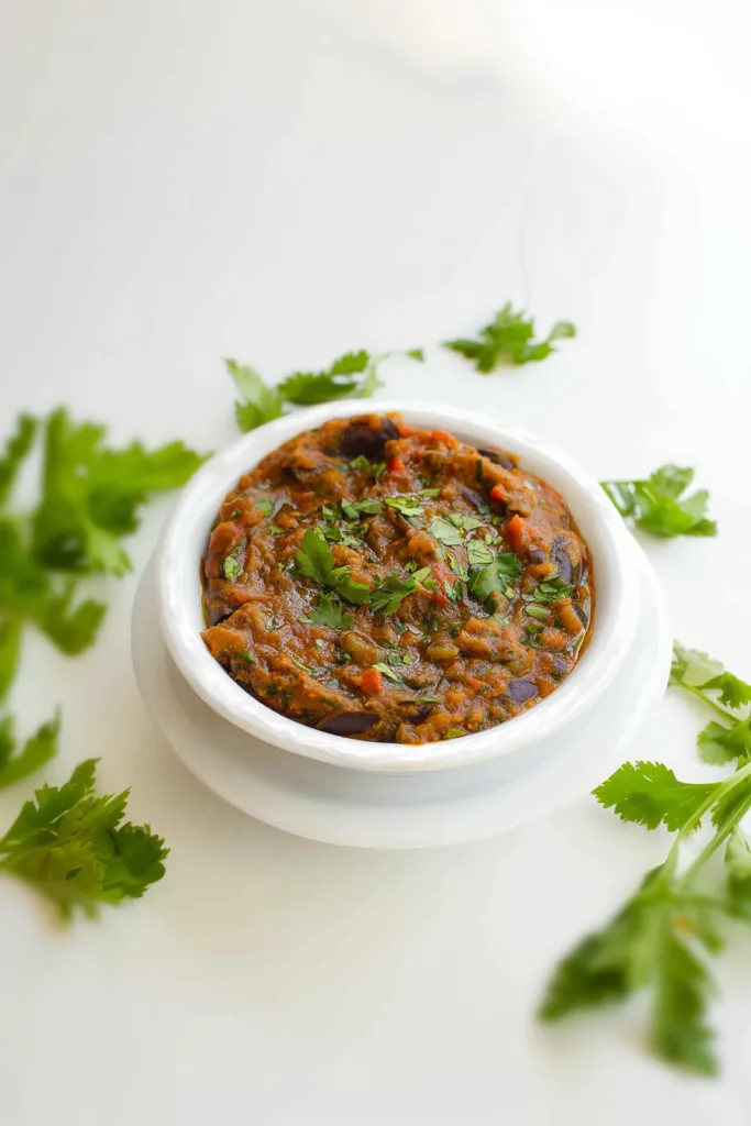 Warm eggplant and tomato stew presented in a simple white dish, garnished with herbs.