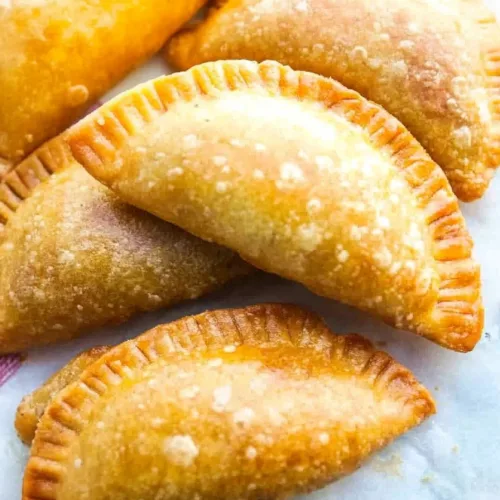 Golden-brown fried empanadas arranged on parchment paper, showing crisp, blistered surfaces.
