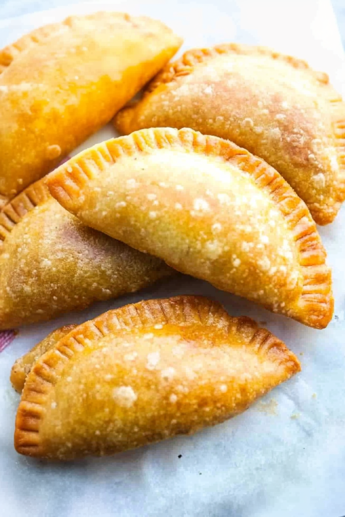 Golden-brown fried empanadas arranged on parchment paper, showing crisp, blistered surfaces.