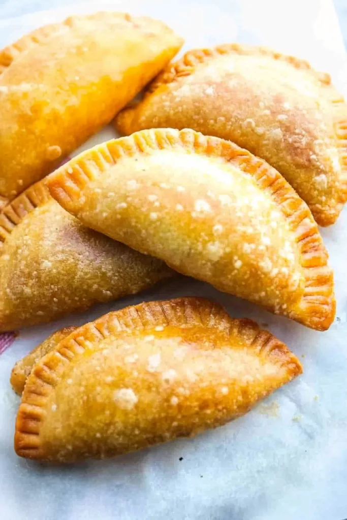 Golden-brown fried empanadas arranged on parchment paper, showing crisp, blistered surfaces.