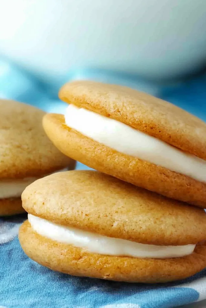 Soft golden sandwich cookies with thick white cream filling, styled against a blue cloth.